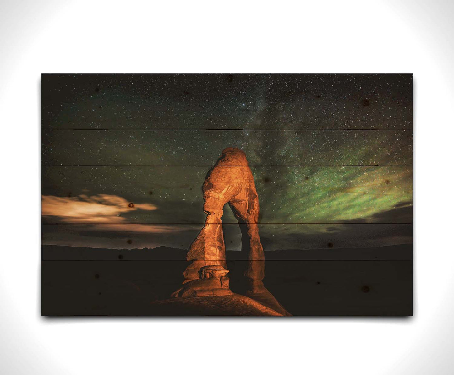 Nighttime photo of Delicate Arch in Arches National Park, Utah. The arch is lit with staged lighting, with a backdrop of a starry night sky. Printed on a wood pallet.