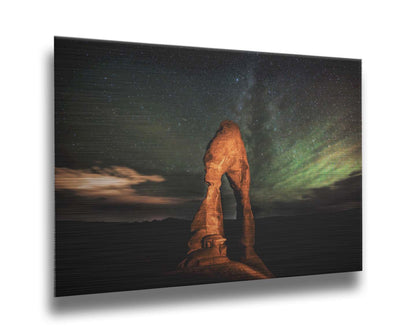 Nighttime photo of Delicate Arch in Arches National Park, Utah. The arch is lit with staged lighting, with a backdrop of a starry night sky. Printed on metal.