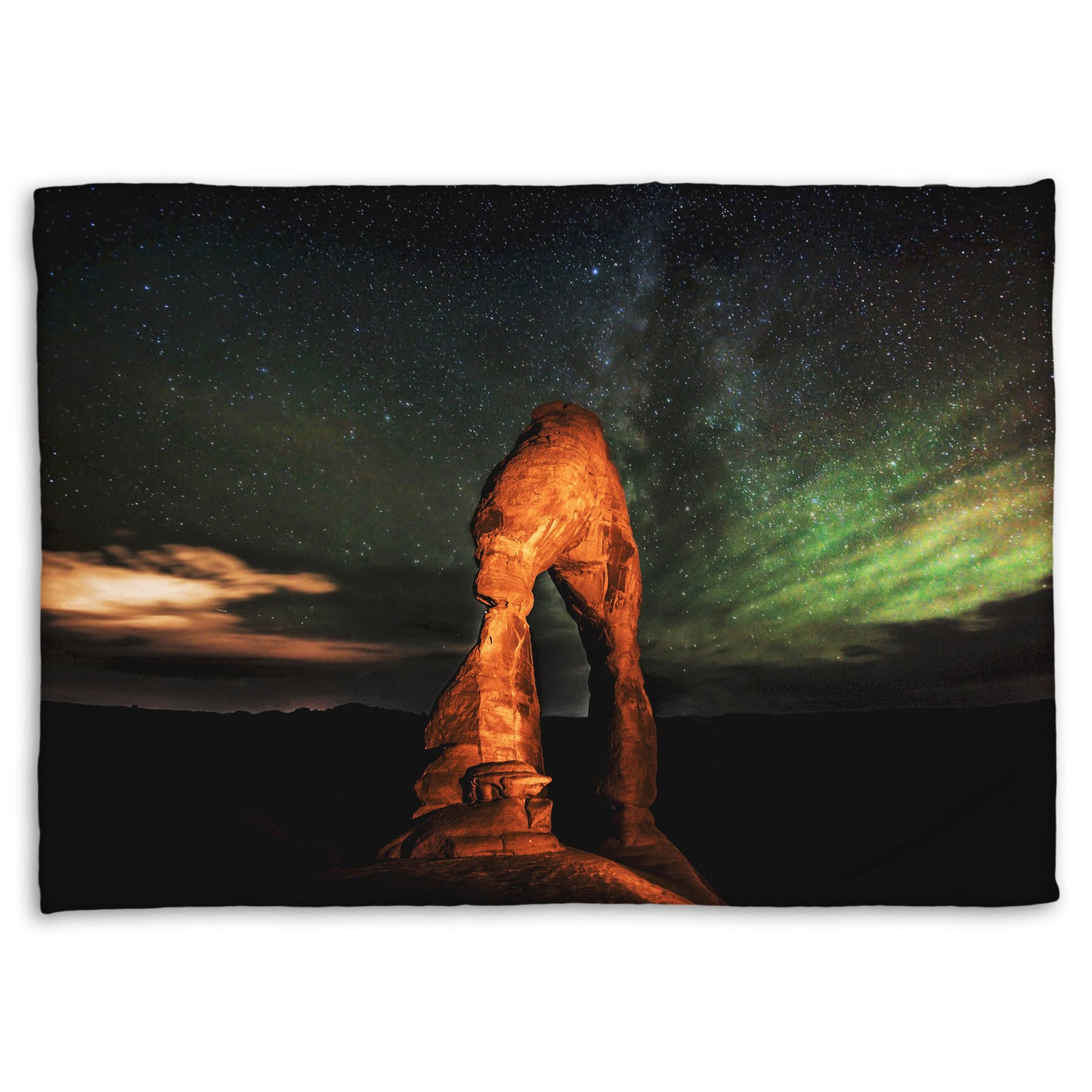 Coral fleece blanket designed with a nighttime photo of Delicate Arch in Arches National Park, Utah. The arch is lit with staged lighting, with a backdrop of a starry night sky.