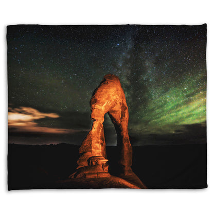 Coral fleece blanket designed with a nighttime photo of Delicate Arch in Arches National Park, Utah. The arch is lit with staged lighting, with a backdrop of a starry night sky.