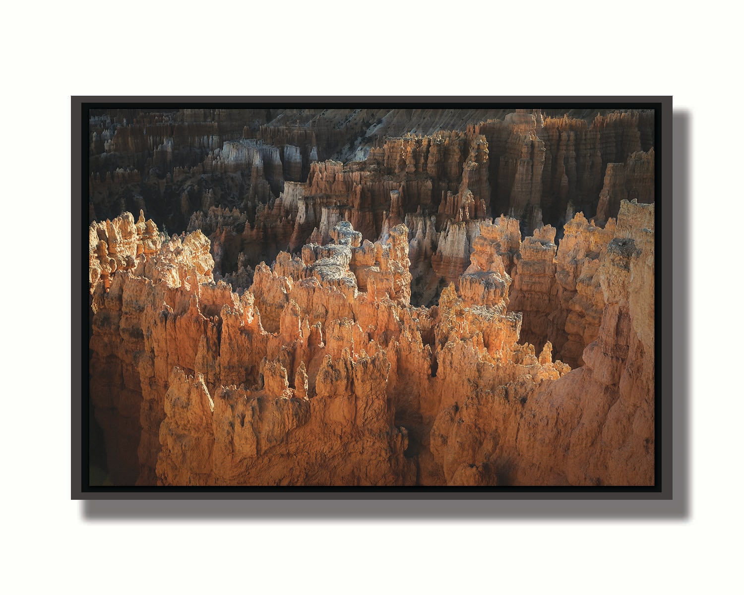 A photo of hoodoo rock formations, jagged stone spires formed by the erosion of a plateau, in Bryce Canyon National Park from a high angle. Printed on canvas in a float frame.