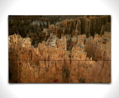 A photo of hoodoo rock formations, jagged stone spires formed by the erosion of a plateau, in Bryce Canyon National Park from a high angle. Printed on a wood pallet.