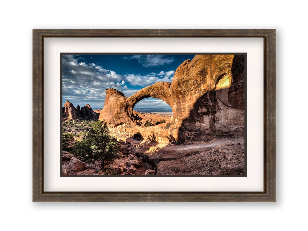 Photo of the Double O arch in the Devil's Garden at Arches National Park, Utah. The rocky arch is set against a bright blue sky. Printed on paper, matted, and framed.