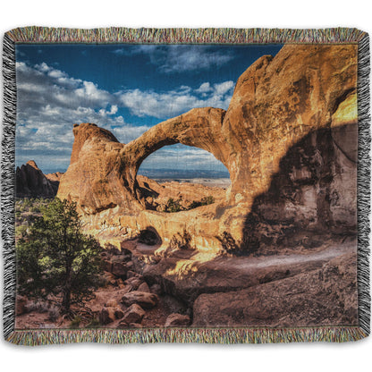 Woven throw blanket designed with a photo of the Double O arch in the Devil's Garden at Arches National Park, Utah. The rocky arch is set against a bright blue sky.