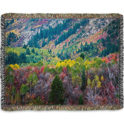 A woven throw blanket designed with a photo looking down on a forest at the Sundance Mountain Resort in Utah. The trees are changing colors, ranging from green, yellow, and red to no leaves at all.