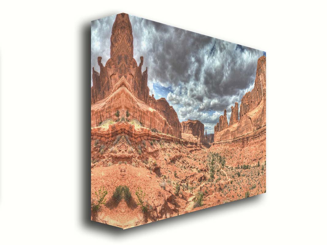 A photo of a tan, sandy, rocky valley along the Park Avenue hiking trail at Arches National Park in Utah. Gray and white clouds fill the sky. Printed on canvas.