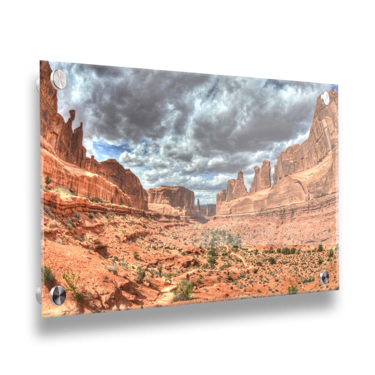 A photo of a tan, sandy, rocky valley along the Park Avenue hiking trail at Arches National Park in Utah. Gray and white clouds fill the sky. Printed on acrylic.