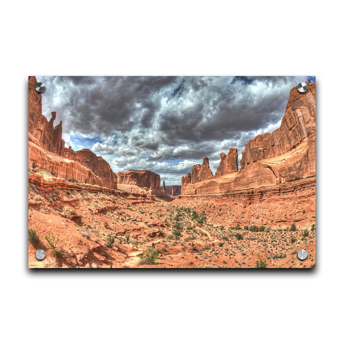 A photo of a tan, sandy, rocky valley along the Park Avenue hiking trail at Arches National Park in Utah. Gray and white clouds fill the sky. Printed on acrylic.