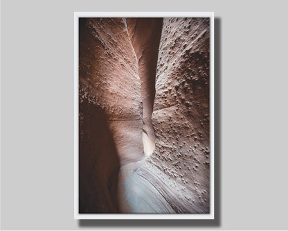 A photo of the slot canyon called Spooky near Escalante, Utah. It features a narrow crevice of lrough and smooth layers of stone. Printed on canvas in a float frame.