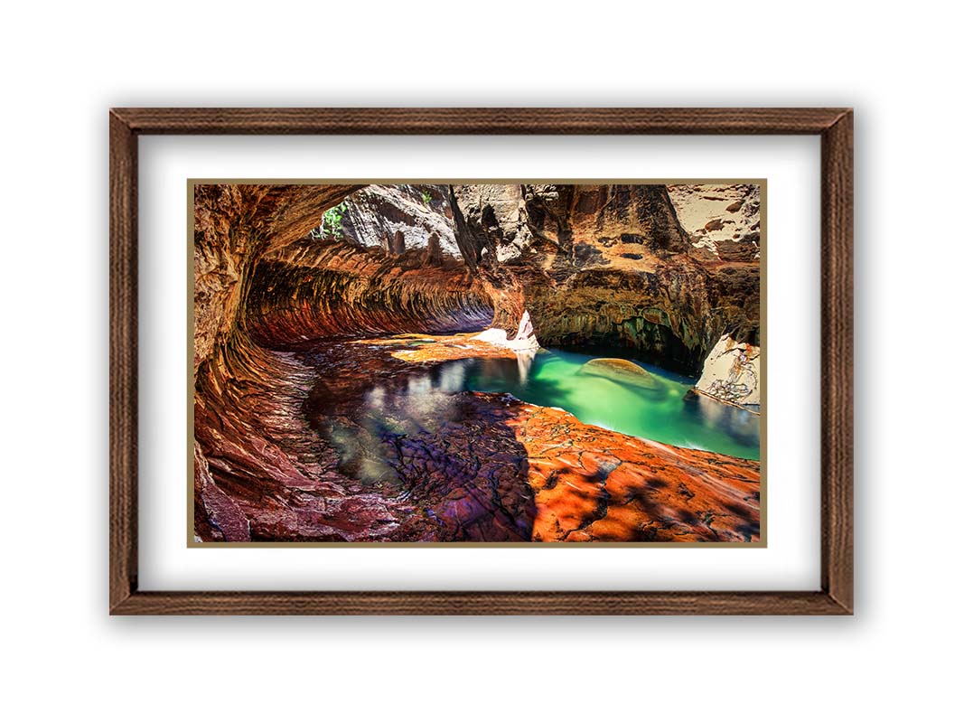 A photo from inside The Subway, or Left Fork of North Creek, at Zion National Park in Utah. It features a canyon of orange and red stone with a vibrant pool of green waters. Printed on paper, matted, and framed.