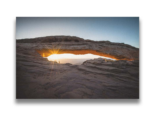 Photo of a stone arch from a national park in Utah. The sunrise site just between the horizon and the underside of the arch, creating a beautiful orange highlight to the underside of the stone structure. Printed on canvas.