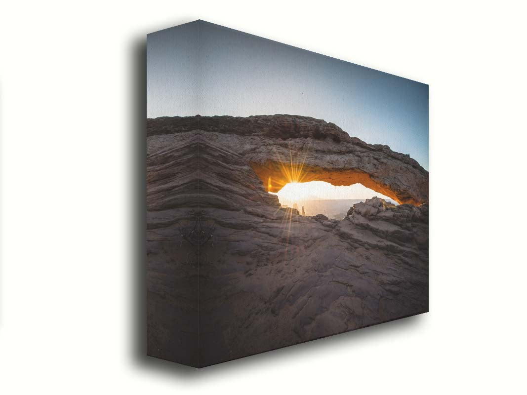 Photo of a stone arch from a national park in Utah. The sunrise site just between the horizon and the underside of the arch, creating a beautiful orange highlight to the underside of the stone structure. Printed on canvas.