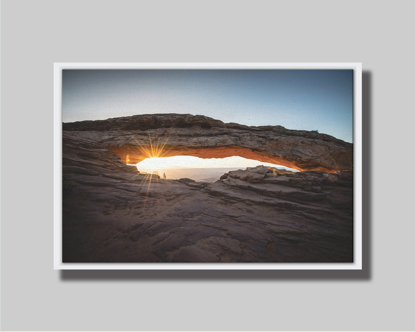 Photo of a stone arch from a national park in Utah. The sunrise site just between the horizon and the underside of the arch, creating a beautiful orange highlight to the underside of the stone structure. Printed on canvas in a float frame.