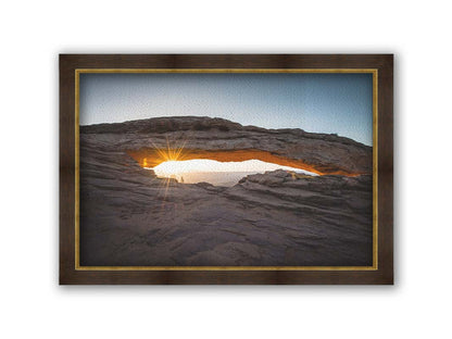 Photo of a stone arch from a national park in Utah. The sunrise site just between the horizon and the underside of the arch, creating a beautiful orange highlight to the underside of the stone structure. Printed on canvas and framed.