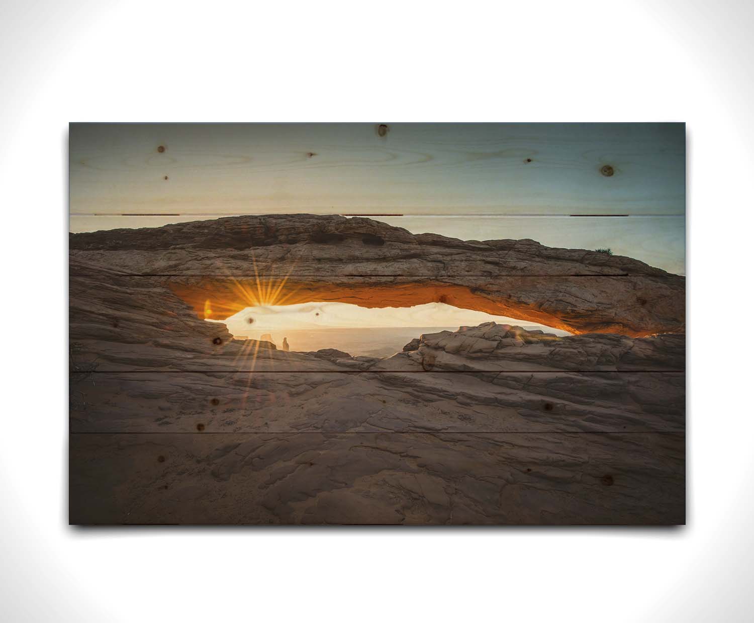 Photo of a stone arch from a national park in Utah. The sunrise site just between the horizon and the underside of the arch, creating a beautiful orange highlight to the underside of the stone structure. Printed on a wood pallet.