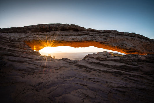 Photo of a stone arch from a national park in Utah. The sunrise site just between the horizon and the underside of the arch, creating a beautiful orange highlight to the underside of the stone structure.