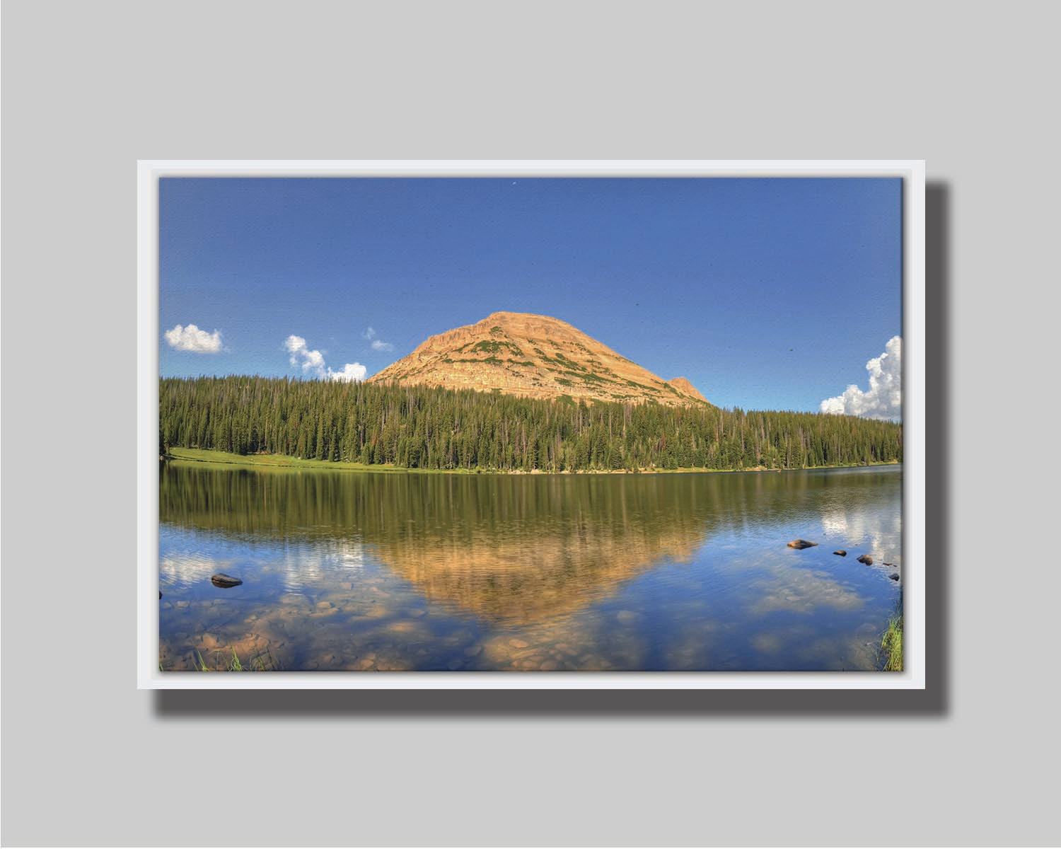 Photo of Mirror Lake in Utah. A mountain, forest, blue sky, and fluffy clouds are reflected on the lakewater. Printed on canvas in a float frame.