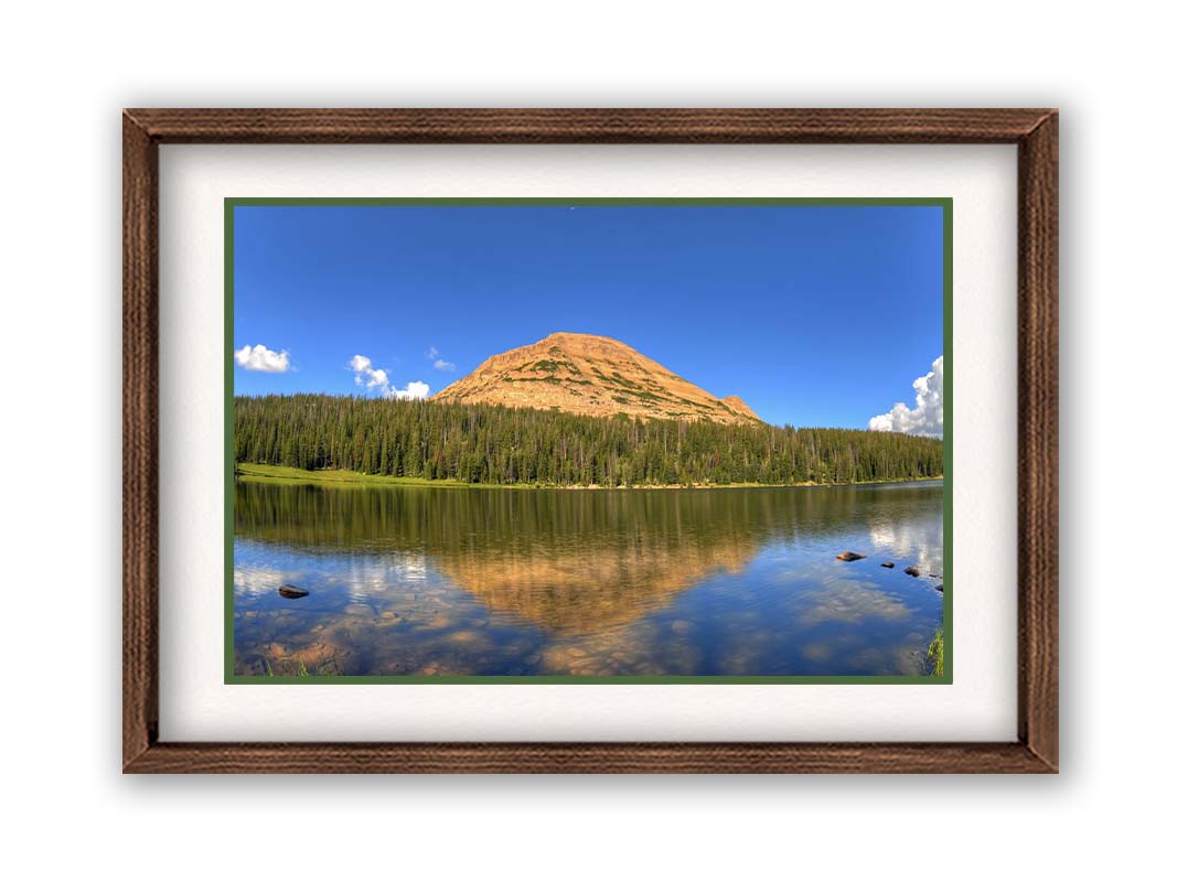 Photo of Mirror Lake in Utah. A mountain, forest, blue sky, and fluffy clouds are reflected on the lakewater. Printed on paper, matted, and framed.