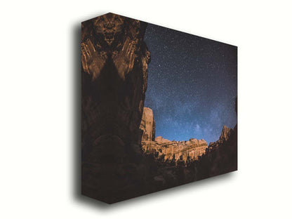 A photo of a clear, starry night sky from the Capitol Reef National Park. The stony plateaus encircle the view of the stars. Printed on canvas.