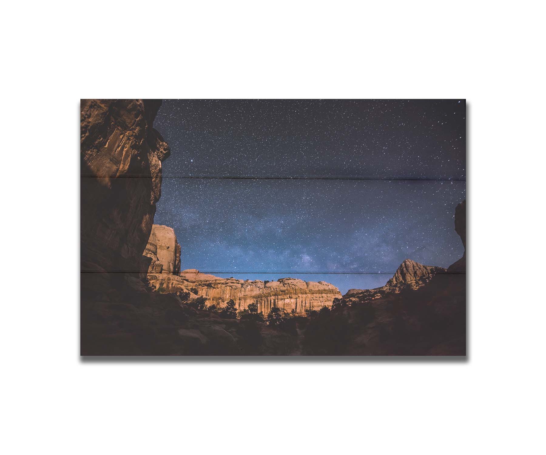 A photo of a clear, starry night sky from the Capitol Reef National Park. The stony plateaus encircle the view of the stars. Printed on a box board.