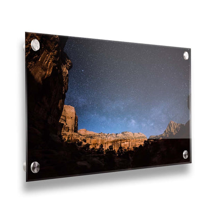 A photo of a clear, starry night sky from the Capitol Reef National Park. The stony plateaus encircle the view of the stars. Printed on acrylic.