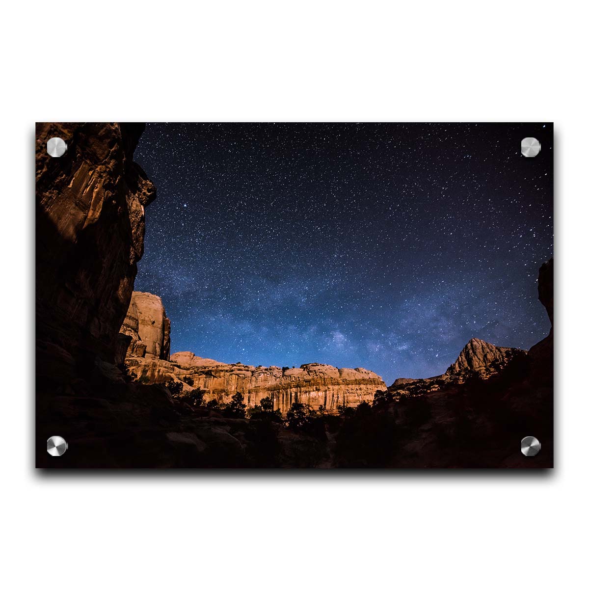 A photo of a clear, starry night sky from the Capitol Reef National Park. The stony plateaus encircle the view of the stars. Printed on acrylic.