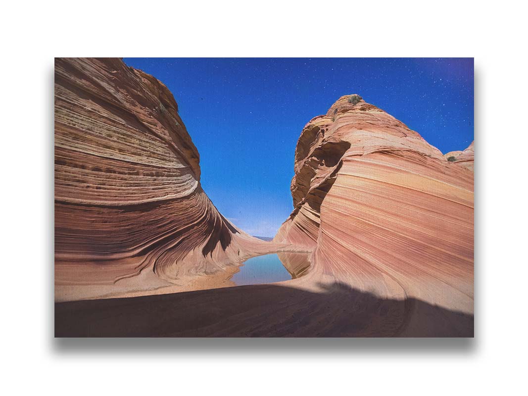 Photo of the "Wave" rock formation at Coyote Buttes North in Utah. A bright night shot captures stripes of sandstone layers forming orange waves against a starry blue sky. Printed on canvas.