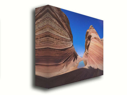 Photo of the "Wave" rock formation at Coyote Buttes North in Utah. A bright night shot captures stripes of sandstone layers forming orange waves against a starry blue sky. Printed on canvas.