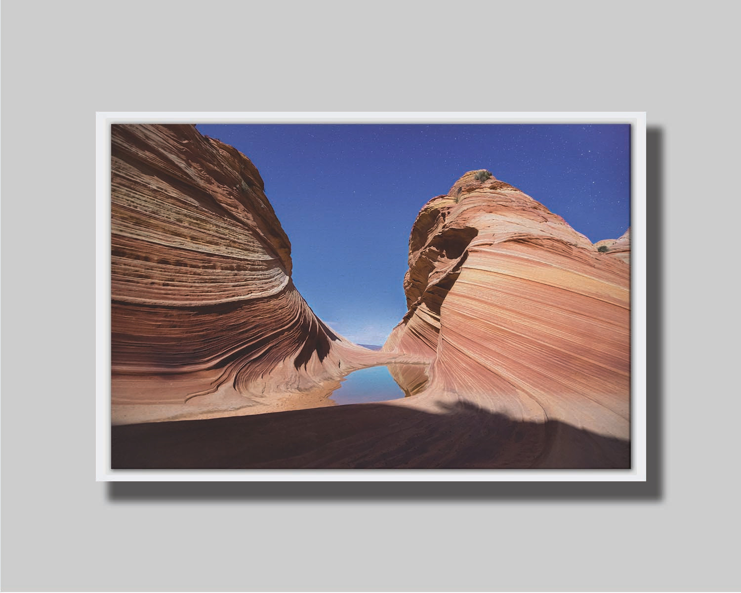 Photo of the "Wave" rock formation at Coyote Buttes North in Utah. A bright night shot captures stripes of sandstone layers forming orange waves against a starry blue sky. Printed on canvas in a float frame.