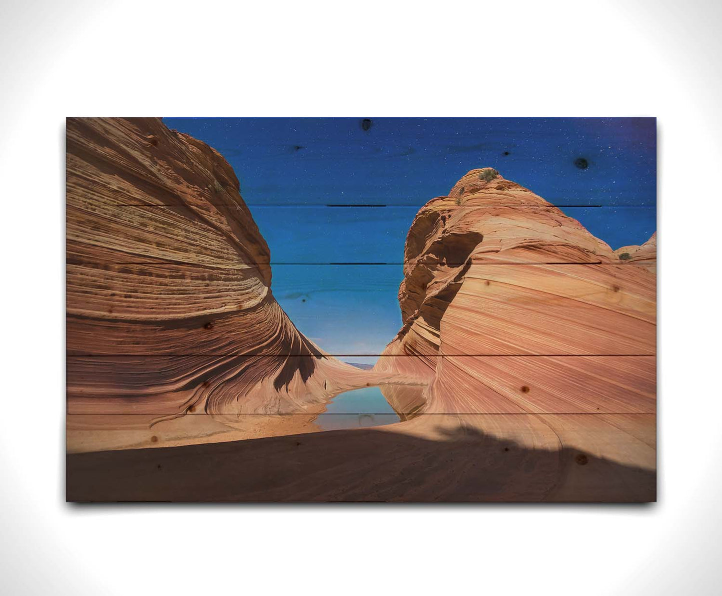 Photo of the "Wave" rock formation at Coyote Buttes North in Utah. A bright night shot captures stripes of sandstone layers forming orange waves against a starry blue sky. Printed on a wood pallet.