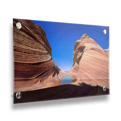 Photo of the "Wave" rock formation at Coyote Buttes North in Utah. A bright night shot captures stripes of sandstone layers forming orange waves against a starry blue sky. Printed on acrylic.