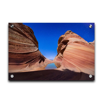 Photo of the "Wave" rock formation at Coyote Buttes North in Utah. A bright night shot captures stripes of sandstone layers forming orange waves against a starry blue sky. Printed on acrylic.