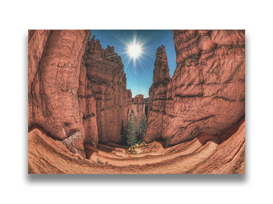 Photo of the Navajo Loop Switchbacks rock formation at Bryce Canyon National Park in Utah. It is taken wit a fish eye lens perspective which emphasizes the height and depth of the structures. A bright blue sky peeks out between parallel walls of red stone, and the bright white rays of the perfectly centered sun shine down between. Printed on canvas.