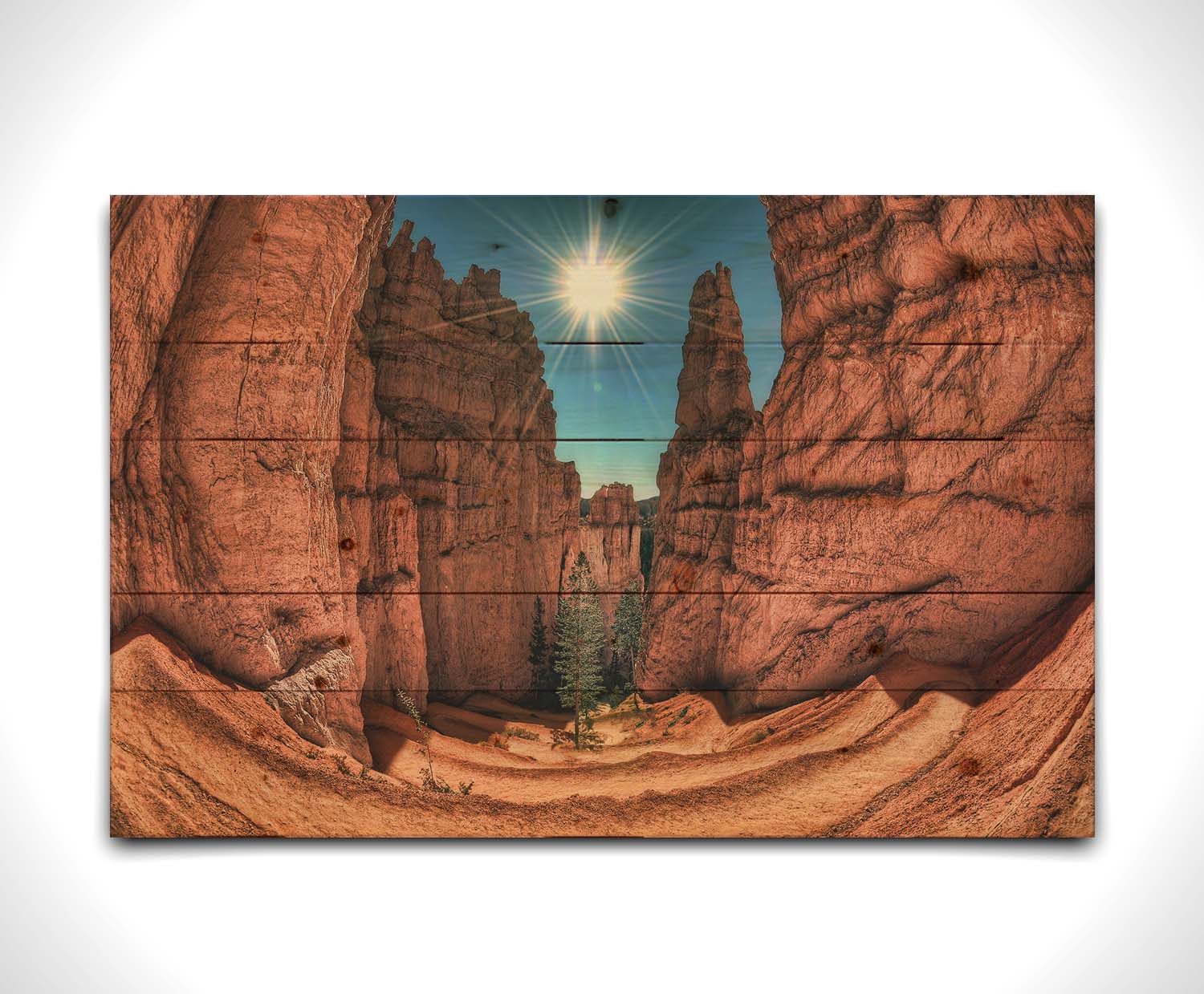 Photo of the Navajo Loop Switchbacks rock formation at Bryce Canyon National Park in Utah. It is taken wit a fish eye lens perspective which emphasizes the height and depth of the structures. A bright blue sky peeks out between parallel walls of red stone, and the bright white rays of the perfectly centered sun shine down between. Printed on a wood pallet.