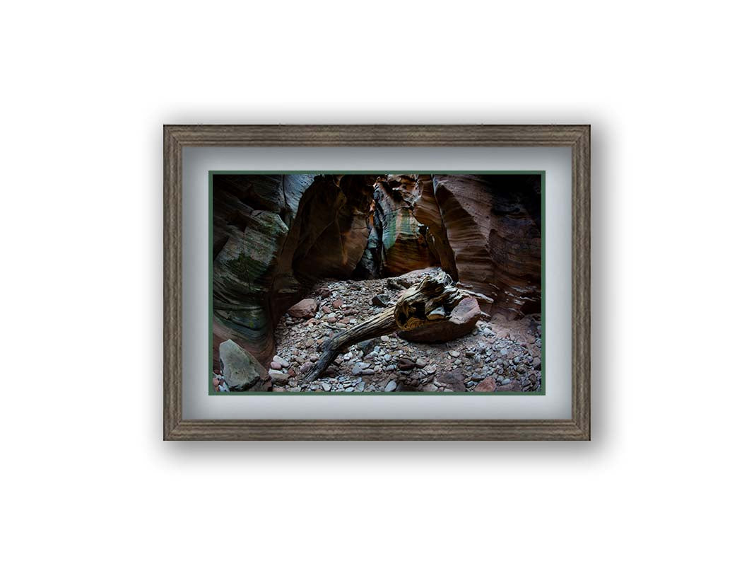 A photo from inside Pine Creek Canyon in Zion National Park, Utah. A piece of driftwood rests on a pile of eroded stones from the cliffaces. Printed on paper, matted, and framed.