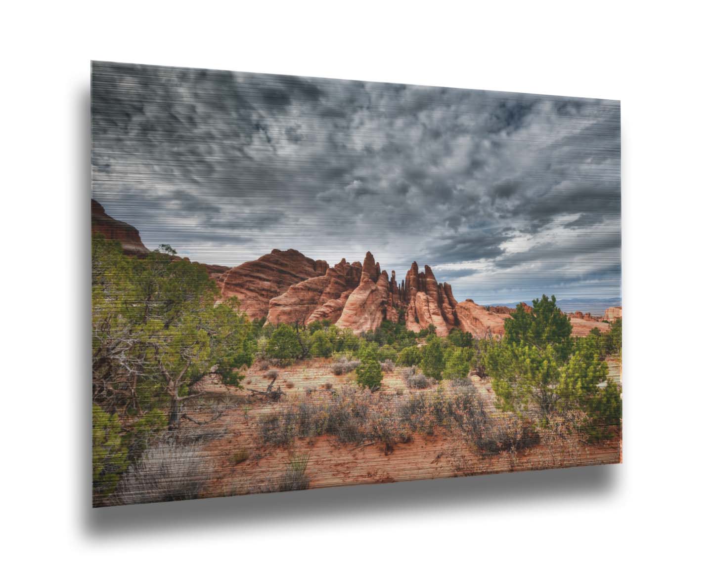 A photo of the Sandstone Fins rock formation in Arches National Park, Utah. The vertical slabs of orange sandstone stand out against the cloudy gray sky. Printed on metal.