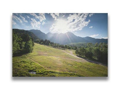 A photo of the sun shining brightly over Mount Timpanogos. The hillsides and forest are the fresh green of springtime. Printed on canvas.