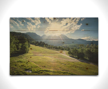 A photo of the sun shining brightly over Mount Timpanogos. The hillsides and forest are the fresh green of springtime. Printed on a wood pallet.