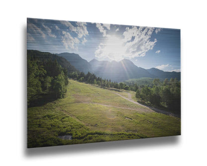 A photo of the sun shining brightly over Mount Timpanogos. The hillsides and forest are the fresh green of springtime. Printed on metal.