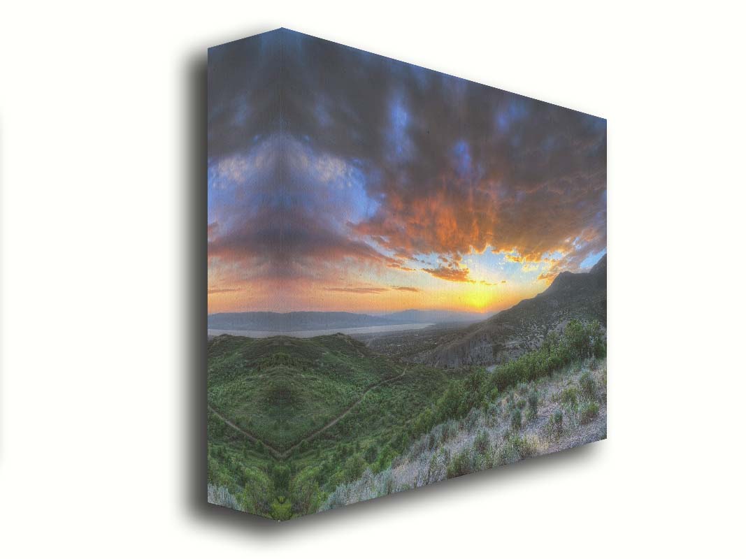 A photo of the sunset at Piestewa Peak in Provo Canyon, Utah. The gold light from the sun reflects off gray clouds about the green foliage surrounding the mountain. Printed on canvas.