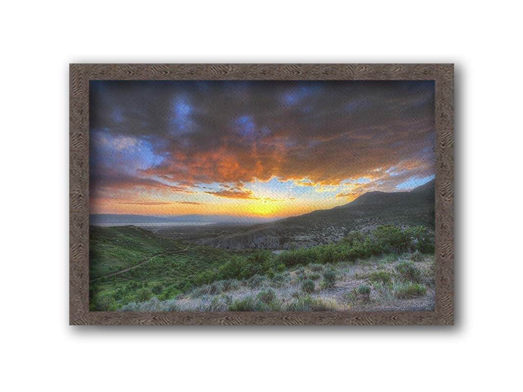 A photo of the sunset at Piestewa Peak in Provo Canyon, Utah. The gold light from the sun reflects off gray clouds about the green foliage surrounding the mountain. Printed on canvas and framed.