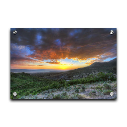 A photo of the sunset at Piestewa Peak in Provo Canyon, Utah. The gold light from the sun reflects off gray clouds about the green foliage surrounding the mountain. Printed on acrylic.