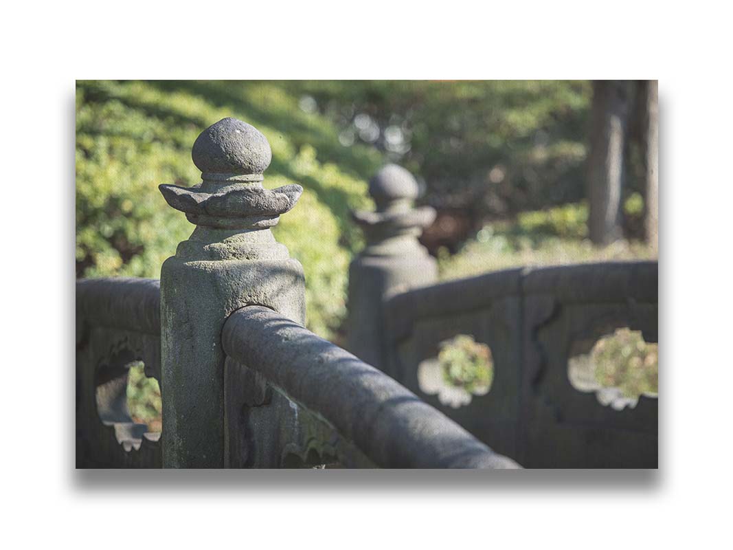 A photo of a detailed stone bridge in Japan, with a background of green plantlife. Printed on canvas.