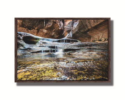 A photo of the Left Fork North Creek flowing through the Subway slot canyon in Utah's Zion National Park. It flows toward the camera, tumbling over slabs in the sandstone to create small waterfalls. Printed on canvas in a float frame.