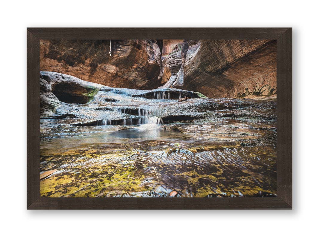 A photo of the Left Fork North Creek flowing through the Subway slot canyon in Utah's Zion National Park. It flows toward the camera, tumbling over slabs in the sandstone to create small waterfalls. Printed on canvas and framed.