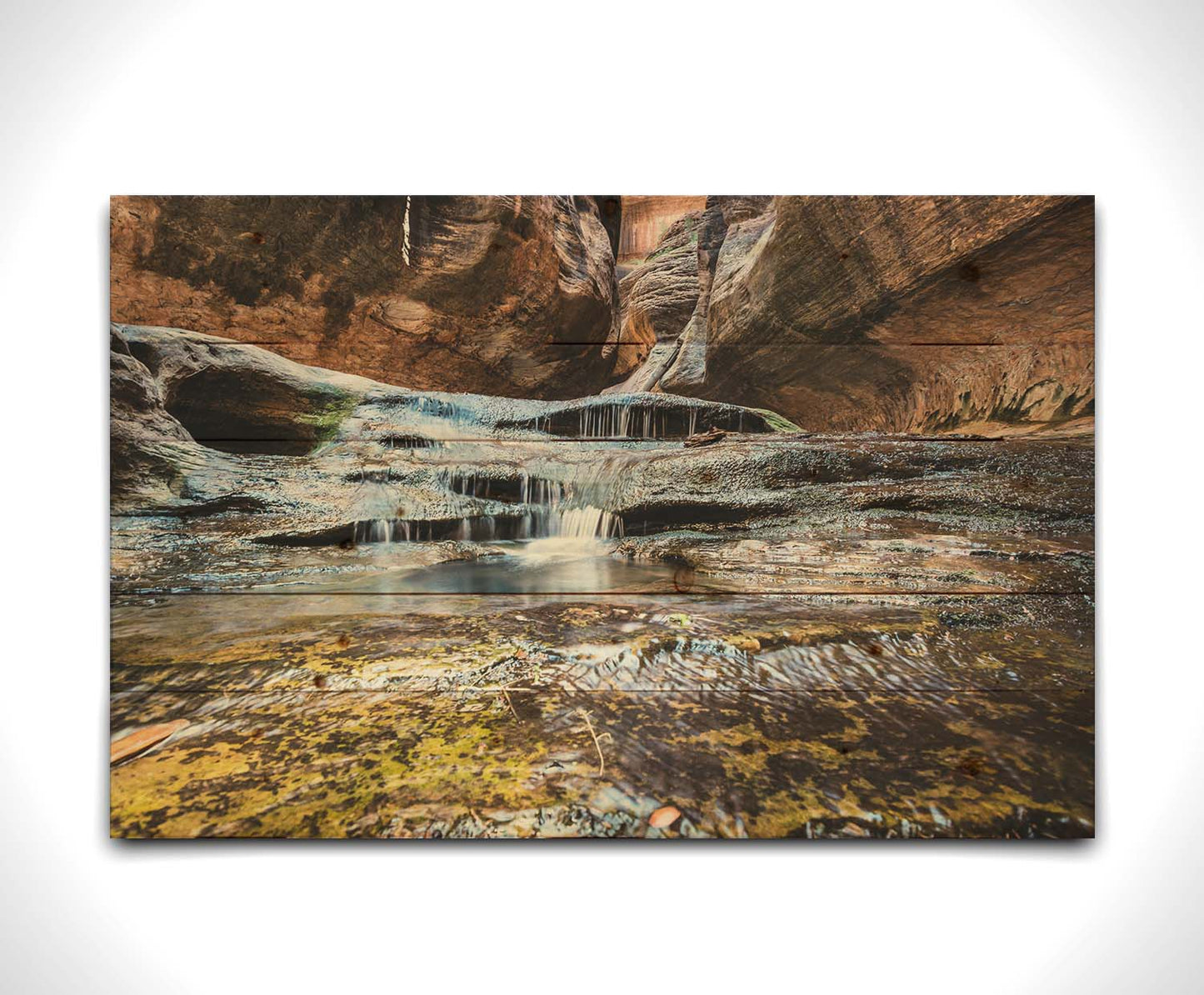 A photo of the Left Fork North Creek flowing through the Subway slot canyon in Utah's Zion National Park. It flows toward the camera, tumbling over slabs in the sandstone to create small waterfalls. Printed on a wood pallet.