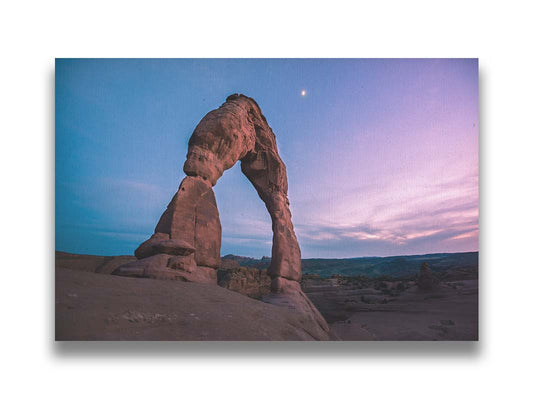 A photo of the Delicate Arch rock formation in Arches National Park, Utah. The blues and purples of the sky at sunset compliment the oranges and browns of the sandstone arch. Printed on canvas.