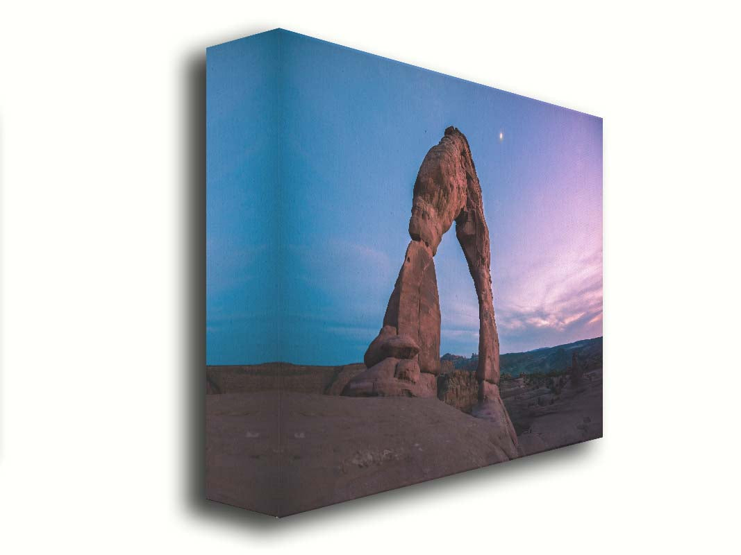 A photo of the Delicate Arch rock formation in Arches National Park, Utah. The blues and purples of the sky at sunset compliment the oranges and browns of the sandstone arch. Printed on canvas.