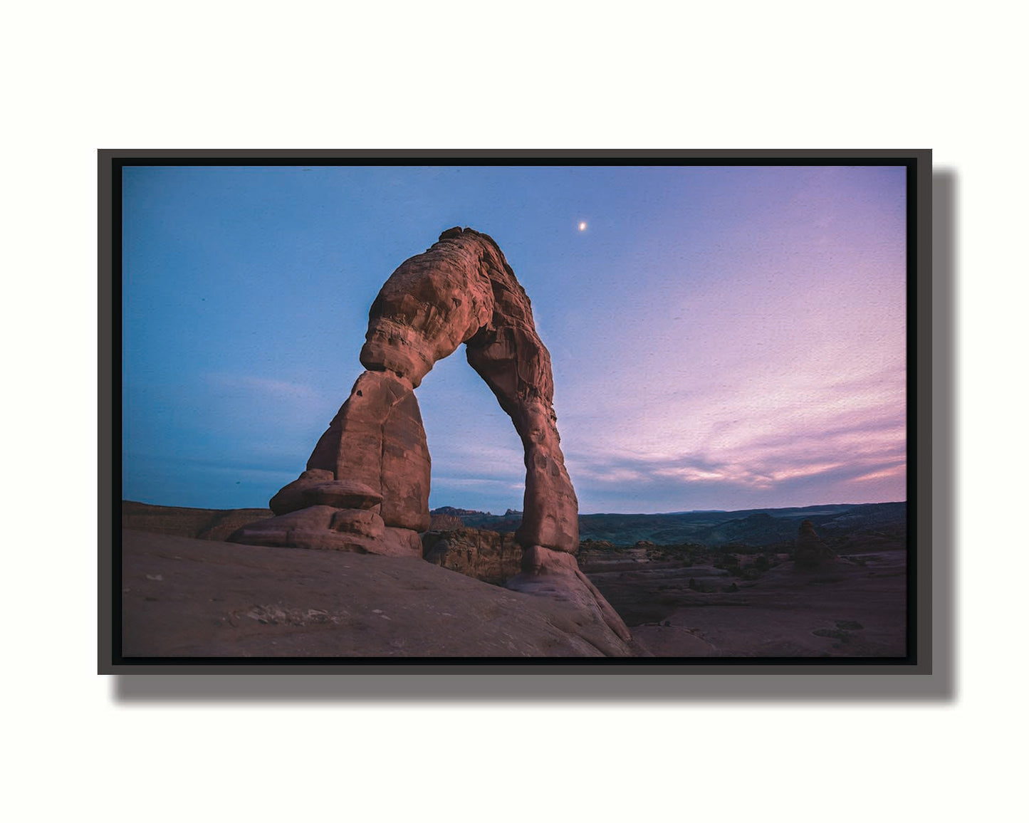 A photo of the Delicate Arch rock formation in Arches National Park, Utah. The blues and purples of the sky at sunset compliment the oranges and browns of the sandstone arch. Printed on canvas in a float frame.