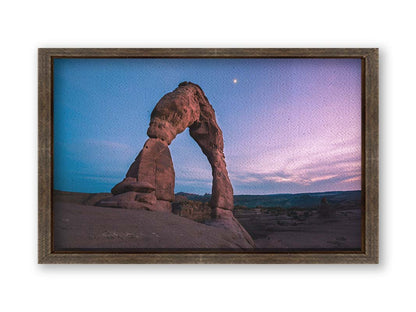 A photo of the Delicate Arch rock formation in Arches National Park, Utah. The blues and purples of the sky at sunset compliment the oranges and browns of the sandstone arch. Printed on canvas and framed.